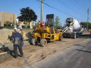 Concrete mixer truck feeding a curb machine along a new roadway