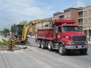 Excavator loading a Vaughan Paving dump truck during urban curb removal