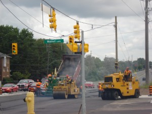 Paving operation underway at a signalized intersection with a roller following