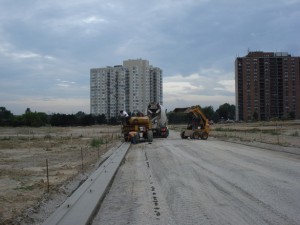 New subdivision roadway under construction with curb machine and apartment towers behind