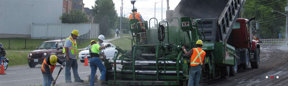 A Vaughan Paving crew laying asphalt behind a VP paver, fed by a dump truck on a city street